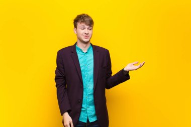 Genç sarışın adam kendini mutlu hissediyor ve gülümsüyor. Bir objeye ya da duvara yaslanmış bir konsepte bakıyor.