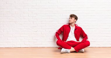 Genç sarışın adam kafası karışık ya da dolu hissediyor ya da şüphe ve sorular, merak ediyor, elleri kalçasında, dikiz aynasıyla yerde oturuyor