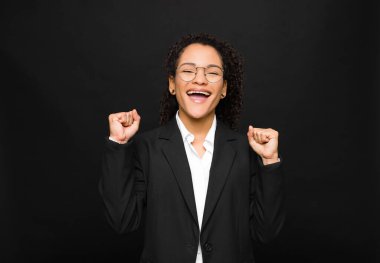 Genç siyah kadın mutlu, pozitif ve başarılı hissediyor, zaferi kutluyor, başarıları kutluyor veya siyah duvara karşı iyi şanslar diliyor.