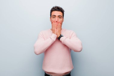 Genç Arap adam şok olmuş ve korkmuş hissediyor. Ağzı açık ve elleri gri duvarda.