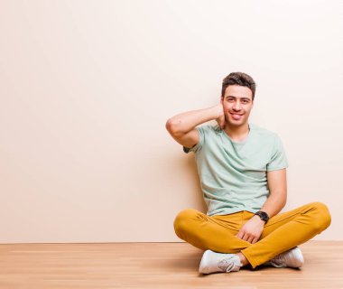 Genç Arap bir adam neşeli ve kendinden emin bir şekilde gülüyor. Sıradan, mutlu, dostane bir gülümsemeyle yerde oturuyor.