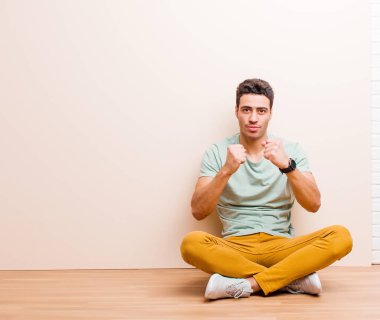 Genç Arap adam kendinden emin, sinirli, güçlü ve agresif görünüyor. Yumrukları boks pozisyonunda dövüşmeye hazır ve yerde oturuyor.