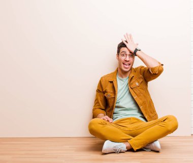 young arabian man raising palm to forehead thinking oops, after making a stupid mistake or remembering, feeling dumb sitting on the floor