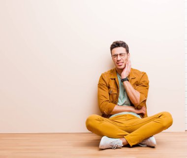 Genç Arap adam, yanağını tutuyor ve ağrılı diş ağrısı çekiyor, hasta, sefil ve mutsuz hissediyor, yerde oturan bir dişçi arıyor.