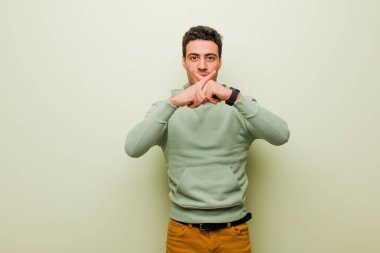 Genç Arap adam ciddi görünüyor ve iki parmağının önde olması hoşnutsuzca reddedilerek düz duvara karşı sessizlik istiyor.