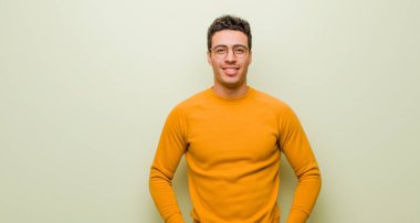 Genç Arap adam sevinçle gülümsüyor. Olumlu, mutlu, kendine güvenen ve yassı duvara karşı gevşek bir ifadeyle.