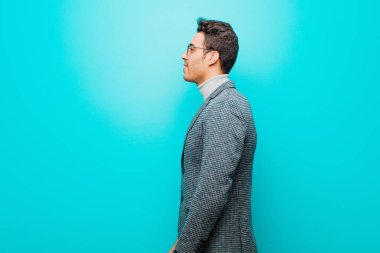 Profil görünümlü genç Arap adam uzayı kopyalamaya çalışıyor, düşünüyor, hayal ediyor ya da mavi duvara karşı hayal kuruyor.