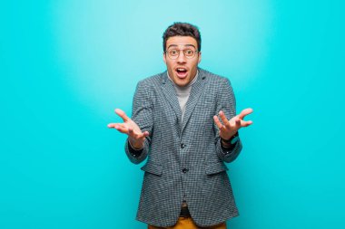 Genç Arap adam mavi duvara karşı inanılmaz bir sürprizle şaşkın ve şaşkın ve şaşkın.