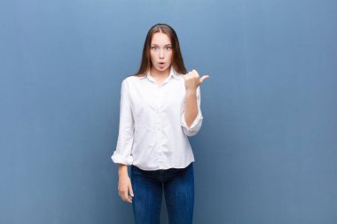 Genç sarışın güzel kız inanamadığı için hayrete düşmüş, yan taraftaki objeyi işaret ediyor ve 