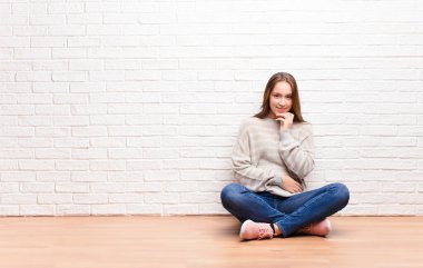 Genç sarışın güzel kız mutlu görünüyor ve gülümsüyor. Elleri çenesinde, merak ediyor ya da soru soruyor. Yerde oturmuş seçenekleri karşılaştırıyor.