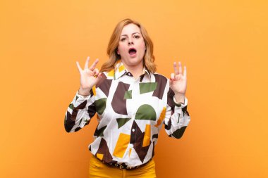 Orta yaşlı kadın şok olmuş, şaşırmış ve şaşırmış hissediyor. Onaylıyor. İki eliyle de onay işareti yapıyor.