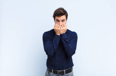 Genç yakışıklı adam endişeli, gergin, stresli ve korkmuş görünüyor, tırnaklarını yiyor ve mavi duvara karşı yanal fotokopi alanı arıyor.