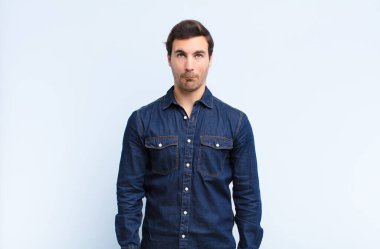 Aptal bakışlı, aptal ve komik görünümlü genç bir adam. Şaşı bakışlı, şakacı ve mavi duvara karşı oynaşan.