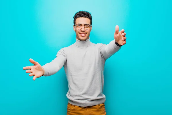 young arabian man smiling cheerfully giving a warm, friendly, loving welcome hug, feeling happy and adorable against flat wall