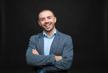 Genç iş adamı mutlu, gururlu ve tatmin olmuş görünüyordu. Kolları düz duvara çaprazlanmış başarılı bir şekilde gülümsüyordu.