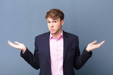 Genç sarışın adam şaşkın ve şaşkın, şüpheci, farklı seçenekleri tartıyor ya da seçiyor. Düz duvara yaslanmış komik bir yüz ifadesi var.