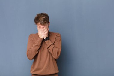 Genç sarışın adam üzgün, hayal kırıklığına uğramış, gergin ve depresif, iki eliyle yüzünü kaplayan, yassı duvara karşı yalnız ağlayan