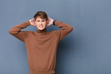 Genç sarışın adam kendini stresli, endişeli, endişeli ya da korkmuş hissediyor, elleri başının üstünde, hatayla panikliyor, yassı duvara yaslanmış.