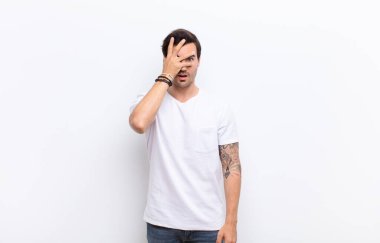 Genç yakışıklı adam şok olmuş, korkmuş ya da korkmuş görünüyor. Yüzü elle kaplanmış ve parmaklarının arasından beyaz duvara bakıyor.