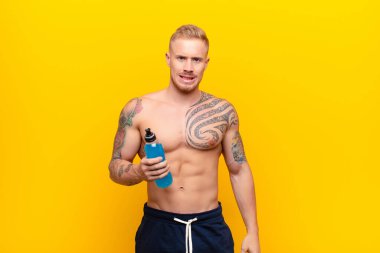 Genç sarışın güçlü adam endişeli, stresli, endişeli ve korkmuş görünüyor. Enerji içeceğiyle panikliyor ve dişlerini sıkıyor.