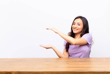 Genç Latin güzel kadın gülümsüyor, mutlu, pozitif ve tatmin olmuş hissediyor, fotokopi odasında düz duvara karşı nesne ya da konsept tutuyor ya da gösteriyor