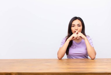 Genç, Latin, güzel bir kadın ciddi görünüyor ve iki parmağının önde olması hoşnutsuzca, reddedilmek üzere, düz duvara karşı sessizlik istiyor.