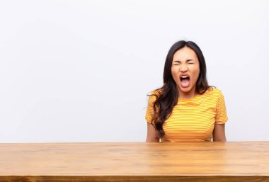 Genç Latin güzel kadın agresif bir şekilde bağırıyor, çok kızgın, hayal kırıklığına uğramış, öfkeli ya da sinirli görünüyor, düz duvara karşı hayır diye bağırıyor.