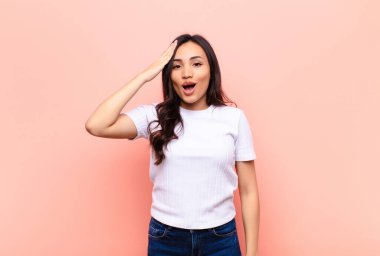 Genç Latin güzel kadın mutlu, şaşkın ve şaşırmış görünüyor, gülümsüyor ve düz duvara karşı inanılmaz ve inanılmaz iyi haberler veriyor.