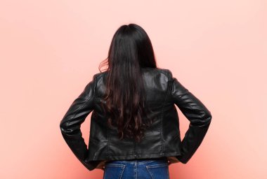 Genç Latin bir kadın kafası karışık ya da dolu hissediyor ya da şüphe ve sorular, merak ediyor, elleri kalçasında, düz duvara karşı dikiz manzaralı