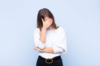 Genç, güzel, İspanyol bir kadın stresli, utanmış ya da üzgün görünüyor. Başı ağrıyor, yüzünü mavi duvara dayamış.