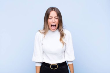 Genç, güzel, İspanyol bir kadın agresif bir şekilde bağırıyor. Kızgın, sinirli, öfkeli ya da sinirli görünüyor. Mavi duvara karşı hayır diye bağırıyor.