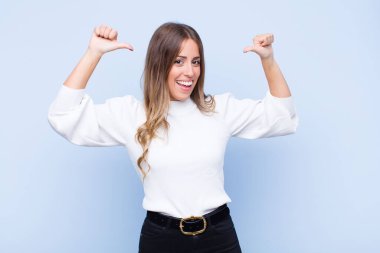 Genç, güzel İspanyol bir kadın gururlu, kibirli ve kendinden emin, tatmin olmuş ve başarılı görünüyor, mavi duvara karşı kendini işaret ediyor.