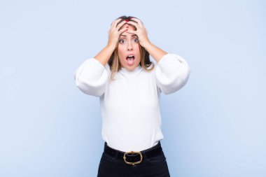 Genç, güzel İspanyol kadın dehşete kapılmış ve şok olmuş hissediyor. Mavi duvara karşı ellerini kaldırıyor ve panikliyor.