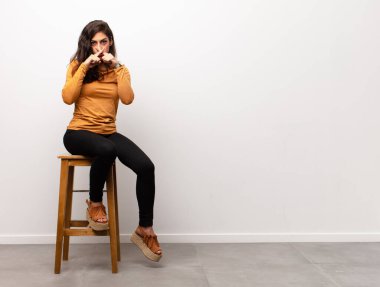 Genç, güzel bir kadın mutlu, heyecanlı ve pozitif hissediyor. Elleri ağızda bağırıyor, bir odaya oturarak bağırıyor.