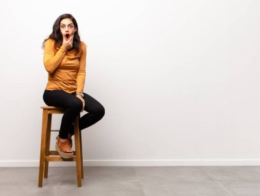 Genç, güzel bir kadın, kafası karışık ya da şüpheci ve soru dolu ellerinin kalçasında, dikiz aynasıyla bir odada oturuyor.