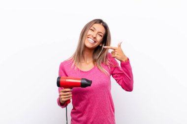 Genç ve güzel bir kadın, kendine güvenerek kendi gülüşünü, pozitif, rahat, saç kurutma makinesiyle tatmin olmuş tavrını gösteriyor..