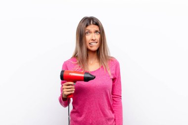 Kafası karışmış ve kafası karışmış genç bir kadın gergin bir hareketle dudağını ısırıyor. Saç kurutma makinesiyle ilgili sorunun cevabını bilmiyor..