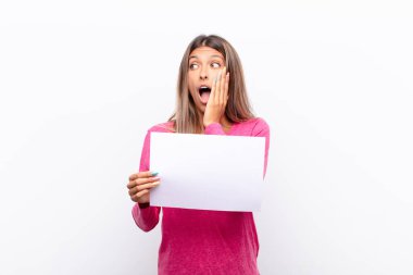 Genç, güzel bir kadın mutlu, heyecanlı ve şaşırmış hissediyor. İki eli yüzü üzerinde bir levhayı tutuyor.