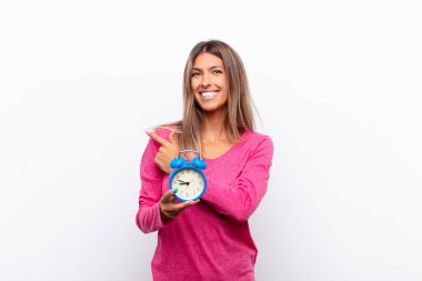 Genç, güzel bir kadın neşeyle gülümsüyor, mutlu hissediyor ve yan ve yukarı doğru işaret ediyor, fotokopi uzayında elinde çalar saat olan bir nesne gösteriyor..