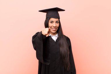 Genç Latin kız öğrenci kameraya tatmin olmuş, kendinden emin, dost canlısı bir gülümsemeyle bakıyor ve seni seçiyor.