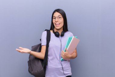 Gri duvara yaslanmış genç, güzel Latin öğrenci kadın.