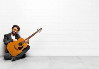 Genç müzisyen pozitif ve kendinden emin gülümsüyor, tatmin olmuş görünüyor, arkadaş canlısı ve gitar, rock 'n roll konseptiyle mutlu.