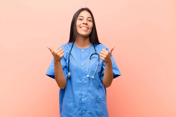 年轻的拉丁裔护士高兴地微笑着 看上去很快乐 双手无忧无虑地靠着粉红的墙壁 显得很积极 — 图库照片
