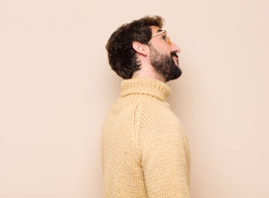 Endişeli, kafası karışık, cahil bir ifadeyle genç, havalı bir adam kopyalama alanına bakıyor, düz duvara karşı şüpheyle bakıyor.