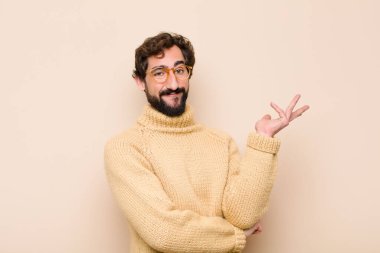 Genç havalı adam gururla ve güvenle gülümsüyor, mutlu ve tatmin olmuş hissediyor ve düz duvara karşı fotokopi alanında bir konsept gösteriyor.