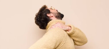 Genç havalı adam yorgun, stresli, endişeli, hayal kırıklığına uğramış ve depresif hissediyor, sırtı ya da boynu düz duvara dayanmış acı çekiyor.