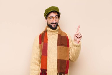 Genç, sakallı, neşeli ve mutlu bir şekilde gülümseyen, tek eliyle uzayı gösteren bir adam.