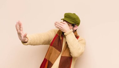 Genç, sakallı, sakallı, yüzü elle kaplayan ve diğer elini kamerayı durdurmak için öne koyan, fotoğraf ya da resimleri reddeden bir adam.