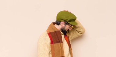 Havalı sakallı genç adam stresli ve hayal kırıklığına uğramış hissediyor, el ele tutuşuyor, yorgun, mutsuz ve migren ağrısı çekiyor.