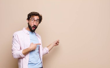 Genç havalı sakallı adam düz duvara karşı bir konsept ifade ediyor.